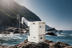 White portable gas water heater with shower hose on rocky coastal rocks, ocean waves and green cliffs in background, no text