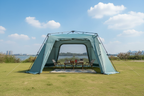 Light blue automatic dome canopy tent in half-open mode on green grass by lake, picnic rug and camping table inside