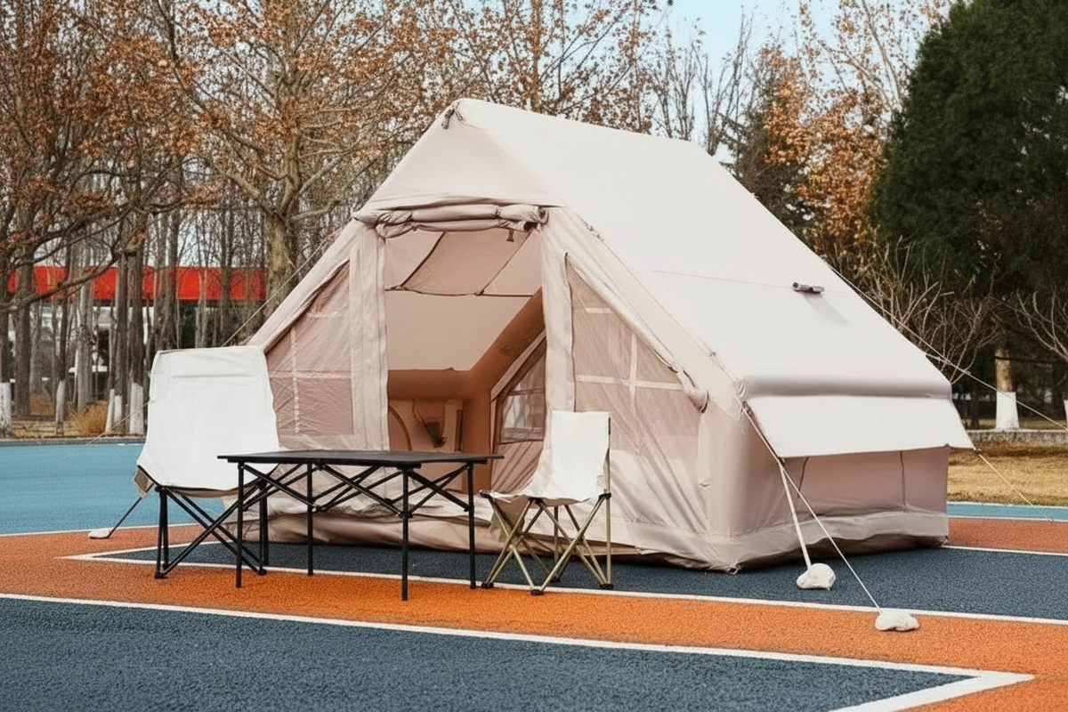 Large beige inflatable ridge tent set up outdoors with folding table and chair in front, no text overlays