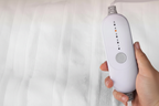 Hand holding white oval electric blanket controller with 5 LED dots and power button, no text or charts