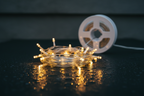 Warm white LED fairy string lights coiled on wet dark surface with water droplets, white hub reel in background, no text