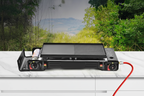 Black portable double burner camping gas stove on white marble surface with forest backdrop, red hose to propane cylinder, no text or watermark