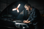 Mechanic working under car hood illuminated by orange LED work light magnetically attached, no text overlays