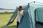 Woman setting up light blue automatic dome canopy tent by pulling support rod, lakeside green grass, no text overlays